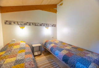 Dos camas individuales con colchas coloridas en una acogedora habitación de Chalet en Camping Des Randonneurs, Francia.