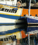 Fishing boats moored at the harbor of Yport, Normandy, France, with colorful reflections in calm water.