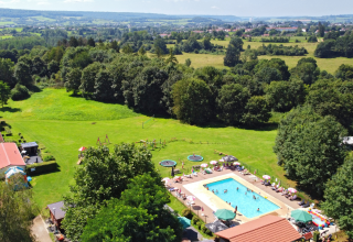 Vista aérea de un alojamiento glamping con piscina, áreas verdes, parque infantil y paisaje arbolado.
