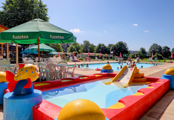 Family-friendly glamping swimming pool with kids’ slide, play area and Fuzetea umbrellas on a sunny day.