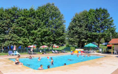 Piscina al aire libre en alojamiento glamping, con huéspedes disfrutando, tumbonas y árboles verdes alrededor.