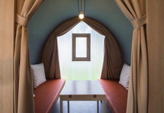 Interior de una tienda safari Coco Sweet en Camping La Colline, Bélgica, con bancos, mesa y ventana.