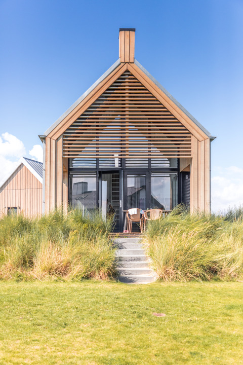 Moderne lodge aan Villa Oesterdam op Oesterdam Resort, Nederland, met houten gevel en hoge grassen.