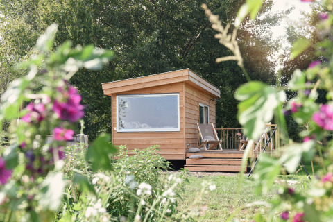 Pequeña casa de madera Smûk Tiny en Smûk Recreatie, Países Bajos, rodeada de flores y vegetación.