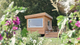 Kleines Holzhaus namens Smûk Tiny bei Smûk Recreatie in den Niederlanden, umgeben von Blumen.