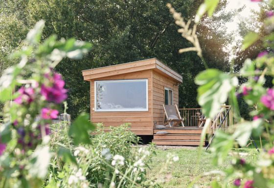 Pequeña casa de madera Smûk Tiny en Smûk Recreatie, Países Bajos, rodeada de flores y vegetación.
