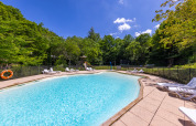 Udendørs swimmingpool med liggestole og grønne træer i baggrunden på Camping Des Randonneurs i Occitanie.