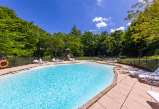 Outdoor swimming pool with sun loungers and lush green trees at Camping Des Randonneurs holiday park in Occitanie.