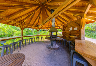 Gazebo coperto in legno con barbecue centrale e sgabelli al Camping Des Randonneurs in Occitania, Francia.