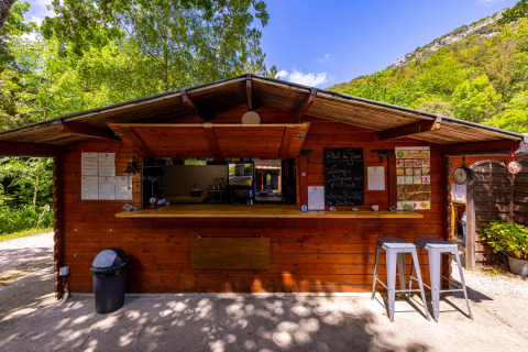 Kiosco de madera en Camping Des Randonneurs en Occitania, Francia, rodeado de vegetación.