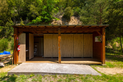 Sanitaires extérieurs en bois entourés de verdure au Camping Des Randonneurs, Occitanie, France.