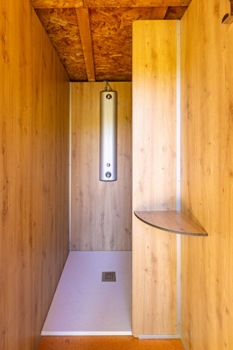 Wood-paneled shower cubicle with modern shower at Camping Des Randonneurs, Occitanie, France.