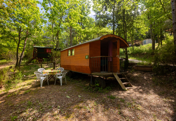 Beeld van een Gipsy wagon zonder privébadkamer bij Camping Des Randonneurs, omringd door bomen.