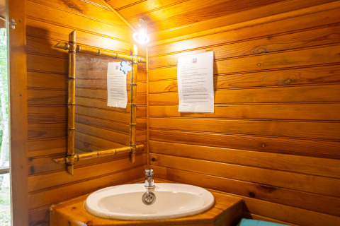 Lavabo y espejo en un baño con paneles de madera de una cabaña en Camping Des Randonneurs, Francia.