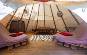 Indvendigt billede af en tipi-telt med senge, trægulv og drømmefangere på Camping Des Randonneurs i Frankrig.