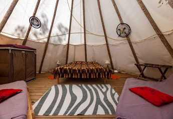 Interno di una tenda tipi con letto matrimoniale, due divani e decorazioni a Camping Des Randonneurs, Francia.