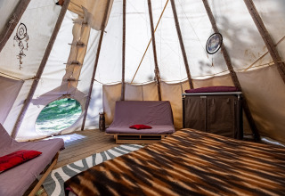 Inde i et teepee-telt med senge, drømmefanger og trærammer på Camping Des Randonneurs i Frankrig.