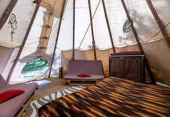Interno di una tenda tipi con letti, acchiappasogni e travi di legno al Camping Des Randonneurs in Francia.