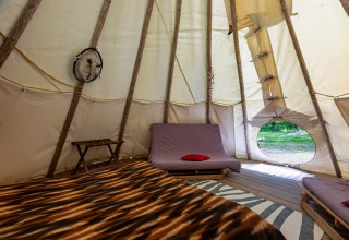 Indvendigt billede af en tipi-telt uden toiletter på Camping Des Randonneurs i Frankrig med senge og tæppe.