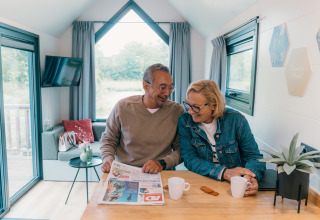 Couple senior partage un café et lit le journal dans une tiny house au Holiday Park Sallandshoeve, Pays-Bas.