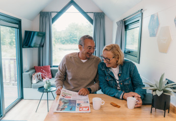 Couple senior partage un café et lit le journal dans une tiny house au Holiday Park Sallandshoeve, Pays-Bas.