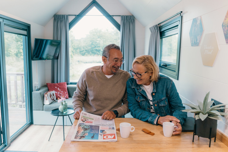 Pareja mayor disfruta de café y periódico en una tiny house del Holiday Park Sallandshoeve, Países Bajos.