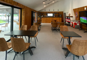 Indendørs caféområde på glampingophold med moderne stole, borde, stort vindue og tv, hyggeligt miljø.