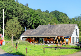 Photo d'un hébergement glamping avec terrasse extérieure, aire de jeux et verdure près d'une colline boisée.