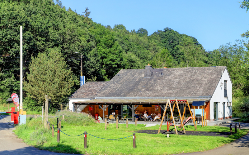 Foto af et glamping-sted med udendørs cafe, legeplads og grønne omgivelser ved en skovbevokset bakke.
