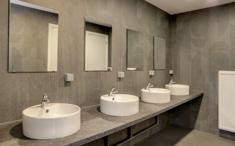 Salle de bains moderne avec quatre lavabos, miroirs et murs gris dans un hébergement glamping chic.