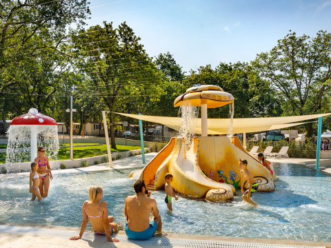 Bambini e adulti si divertono in una piscina con scivolo acquatico e fontana fungo in un villaggio turistico in Croazia.