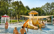 Niños y adultos juegan en una piscina infantil con tobogán y fuente de hongo en un parque vacacional en Croacia.