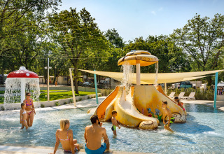 Bambini e adulti si divertono in una piscina con scivolo acquatico e fontana fungo in un villaggio turistico in Croazia.