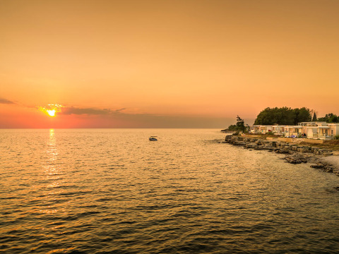 Zonsondergang bij Aminess Planet Camping Maravea Resort in Istrië, Kroatië, met rotsachtige kust en vakantiehuisjes.