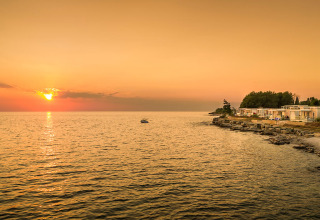 Tramonto sul mare all'Aminess Planet Camping Maravea Resort in Istria, Croazia, con costa rocciosa e bungalow.