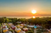 Tramonto su casette e alberi vicino al mare, con piscina e oceano sullo sfondo.