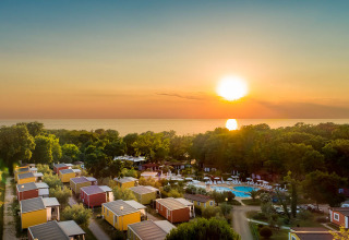Tramonto su casette e alberi vicino al mare, con piscina e oceano sullo sfondo.