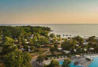 View over Aminess Maravea Camping Resort in Istria, Croatia, featuring pools, RVs, lush trees, and the coast.