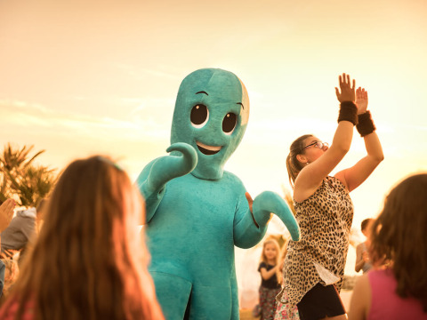 I bambini ballano all'aperto al tramonto con una persona in costume da polpo blu durante una festa allegra.