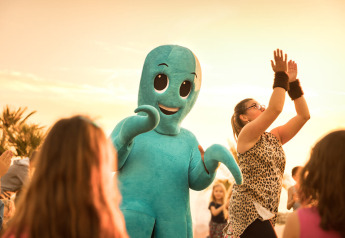 I bambini ballano all'aperto al tramonto con una persona in costume da polpo blu durante una festa allegra.