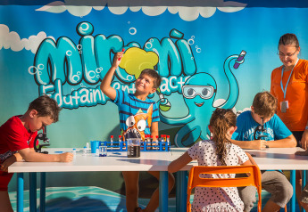 Bambini fanno esperimenti scientifici a un tavolo con un insegnante davanti a una colorata cabina.