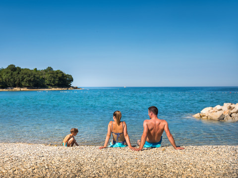 Gezin ontspant op een kiezelstrand bij Aminess Planet Camping Maravea Resort, Istrië, Kroatië.