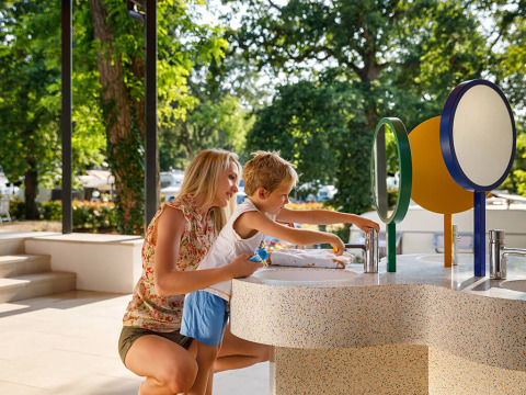 Une mère aide son fils à se laver les mains à des lavabos colorés à Aminess Planet Camping Maravea Resort.
