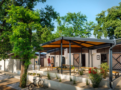 Couple enjoys time in front of stylish bungalows surrounded by trees at Aminess Planet Camping Maravea Resort, Istria.