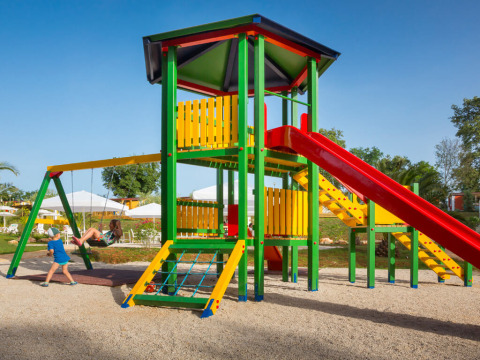 Kinderen spelen op een kleurrijke speeltuin met glijbaan en schommels bij Aminess Planet Camping Maravea Resort in Istrië.