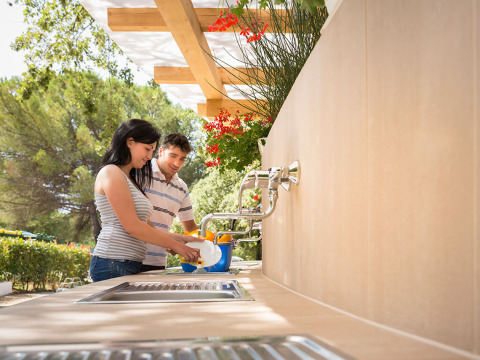 Two people wash dishes outdoors under a pergola at Aminess Planet Camping Maravea Resort in Istria, Croatia.