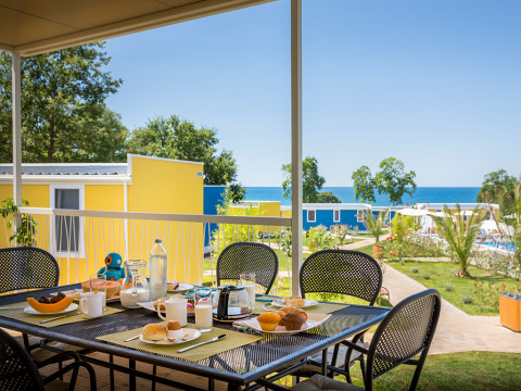 Ontbijttafel buiten met eten en drinken en zicht op kleurrijke chalets en zee in Miramí Family Village.
