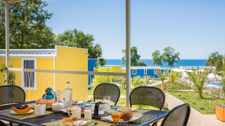 Tavolo da colazione all’aperto con cibo e bevande davanti a casette colorate e vista mare al Miramí Family Village.