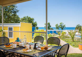 Tavolo da colazione all’aperto con cibo e bevande davanti a casette colorate e vista mare al Miramí Family Village.