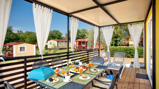 Veranda esterna al Maravea Family Holiday Home con tavolo apparecchiato, tende e vista sui bungalow.
